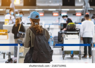 Back View Of Airline Passenger Wear Face Mask To Prevent Corona Virus (Covid-19) Wait To Check In Counter In Airport With Staff Wear Face Mask. New Normal Concept Of Travel After Covid-19 Pandemic.