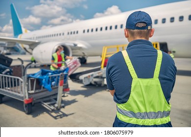 Back view of an airport male worker controlling the luggage uploading onto the conveyor belt