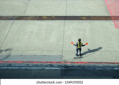 Back View Of Airport Worker Signaling And Directing On Runway Near The Terminal In An Airport, Important Signal.