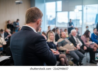 Back View Of Anonymous Businessman In Black Suit Speaking To Audience While Standing On Stage During Business Presentation