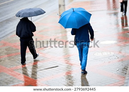 Back view of anonymous commuters walking away on glossy damp pedestrian pavement with geometric red tile patterns during seasonal rain shower. Rainy day. Selective focus