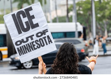 Back view of an anonymous demonstrator holding a handmade “ICE Out of Oahu, Out of Minnesota” sign during a street protest opposing immigration enforcement and deportation policies.