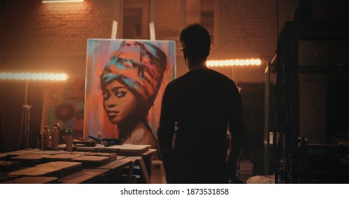 Back view of anonymous man admiring portrait of black woman then walking closer to artwork and applying finishing strokes during work in illuminated workshop - Powered by Shutterstock
