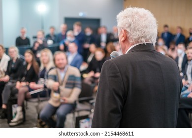 Back View Of Anonymous Senior Businessman In Black Suit Speaking To Audience While Standing On Stage During Business Presentation