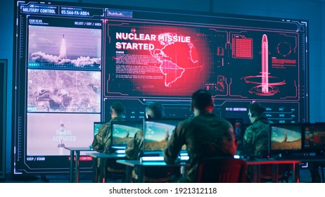 Back view of anonymous soldiers using computers against large screen with count down and online video of nuclear missile launch