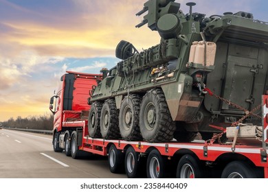Back view armoured personnel carrier stryker with air defense system trailer hauler carrier truck drive military convoy highway road. US troops moving reloceation force reinforcement eastern Europe