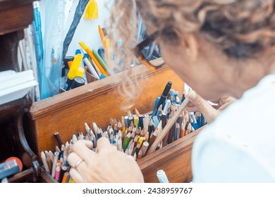 Back view of artist woman at home choosing color pencil to draw and enjoy indoor leisure activity. Creative female people concept lifestyle. Focus on pencils. Hobby at home spending time having fun - Powered by Shutterstock