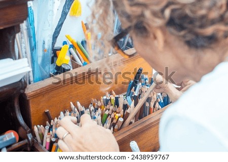 Back view of artist woman at home choosing color pencil to draw and enjoy indoor leisure activity. Creative female people concept lifestyle. Focus on pencils. Hobby at home spending time having fun