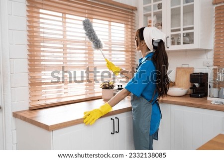 Back view of Asia woman in workwear maid cleaning home and holding dusting brush in her hand, wearing rubber gloves and apron at home