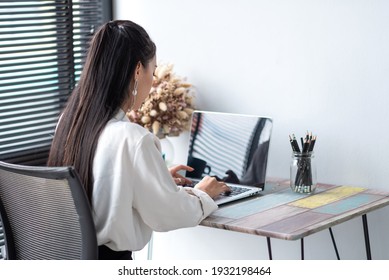 Back View Of An Asian Businesswoman Working On A Laptop Computer At A Wooden Table In The Office.