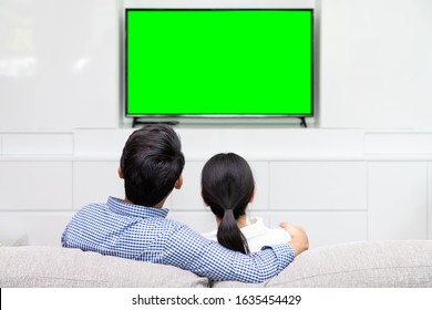 Back View Of Asian Couple Sitting On Sofa Relaxing And Enjoy Watching TV At Home With Green Screen