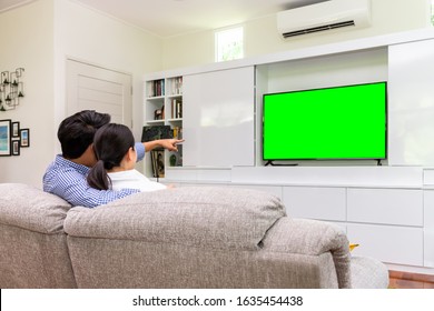 Back view of Asian couple sitting on sofa relaxing and enjoy watching TV at home with green screen