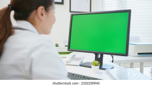 Back View Of Asian Female Doctor Works And Uses Computer With Green Screen Monitor In Hospital