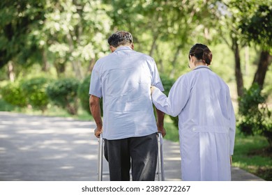 Back view of Asian female doctor helps senior male patient walk to hospital park. Concepts of physicality, caregivers, and therapy. - Powered by Shutterstock