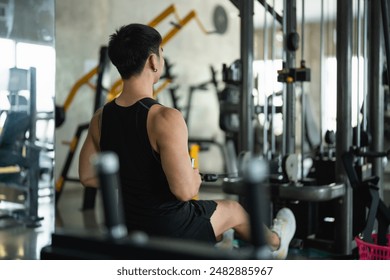 Back view. Asian man in a black tank top works out on a seated row machine in a modern gym. His serious expression and muscular build emphasize his dedication to fitness and strength training. - Powered by Shutterstock