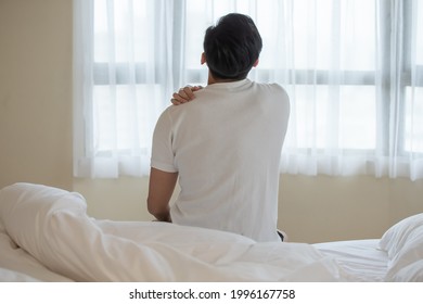 back view of asian man has neck and shoulder pain on bed after wake up in the morning at home