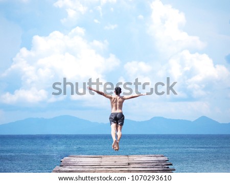Back view of asian man jumping off wooden bridge into blue sea background. Flying freely to the sky. Summer vacation lifestyle.