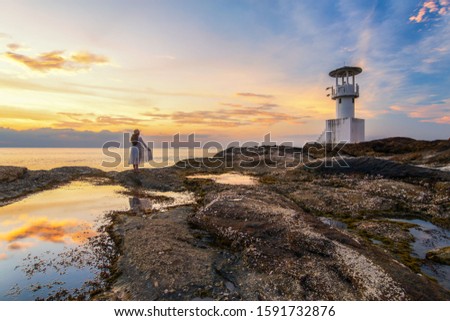 Back view of asian travel woman wearing white dress stand to see sunset at Khao Lak Light Beacon, beautiful sunset time at Nang Thong Beach, Khao Lak, Thailand. Colorful sunset with cloudy sky