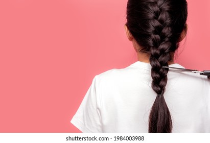 Back view of Asian woman with braided hairstyle is cutting with scissors for donate to cancer patients. Hair donation for breast cancer person. Woman with black long hair braid on pink background.