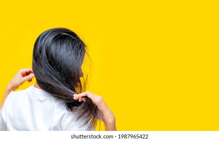 Back view of Asian woman holding damaged hair on yellow background. Hair loss and thin hair problem in woman. Dry and brittle black long hair need shampoo and conditioner for spa treatment.