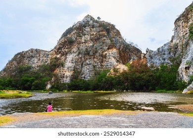 Back view of Asian woman relaxing alone by the lake with beautiful canyon in background. Boy sits on stone alone at riverside with cliffs and beautiful scenery. Relax with beautiful outdoor natural. - Powered by Shutterstock