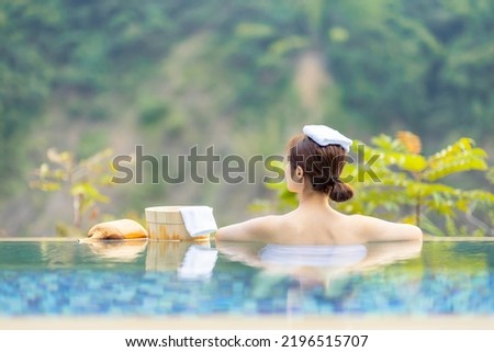 back view of asian woman sitting in hot spring pool relaxing