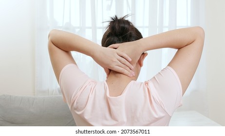 Back view of Asian woman using hands to massage the nape of her neck in physical therapy to reduce pain at work