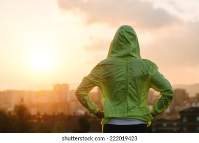 Back view of athlete looking sunset over city skyline after exercising. Motivation, sport and fitness lifestyle concept.
