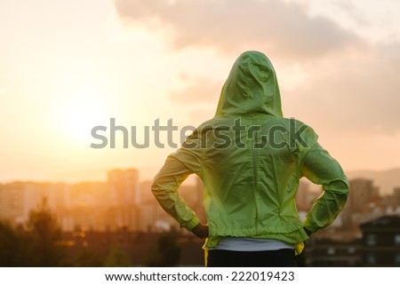 Back view of athlete looking sunset over city skyline after exercising. Motivation, sport and fitness lifestyle concept.
