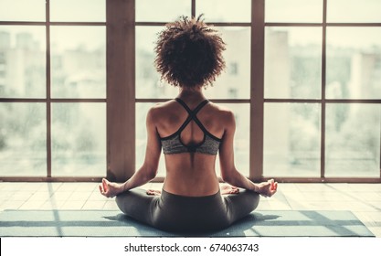 Back view of attractive Afro American girl in sportswear sitting in lotus position while doing yoga