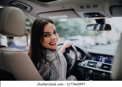 Back View Of An Attractive Business Woman Looking Over Her Shoulder While Driving A Car