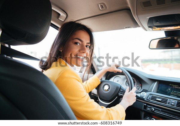 Back view of an attractive\
young business woman looking over her shoulder while driving a\
car
