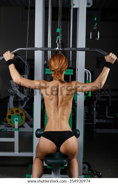 Back view of attractive young topless girl exercising in gym.