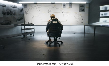 Back View Of Automotive Male Designer Looking At Sketch Blueprint Of Futuristic Electric Car Future Design On Whiteboard. He Sitting On Chair In Modern Car Design Development Studio.