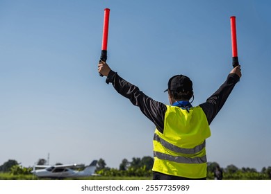 Back view aviation traffic controller man signaling for small plane landing