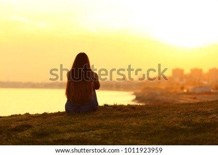 Back view backlight portrait of a single woman watching a sunset on the city with a warm light in the background