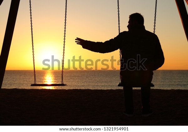 Back\
view backlighting silhouette of a man sitting on swing alone\
missing her partner at sunset on the beach in\
winter