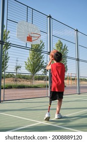 Back view of a basketball kid player with a leg prosthesis throwing the ball to the basket. Shooting basketball.