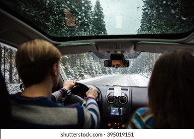 Back view of beautiful couple driving in car through winter forest