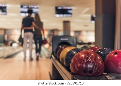 Back view of beautiful girl and handsome guy holding bowling balls and hugging while playing