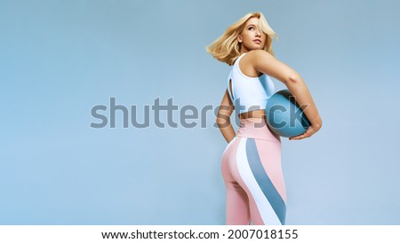 Back view of beautiful girl stretching body holding ball. Female in leggins and white topic sportswear. Copy free space, fitness and sport concept picture.