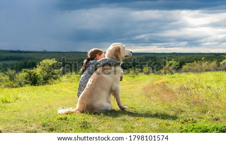Back view of beautiful little girl hugging loyal dog in nature