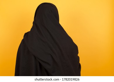 The Back View Of A Beautiful Middle Aged Muslim Woman Wearing Black Hijab Over Yellow Background Studio Shoot.