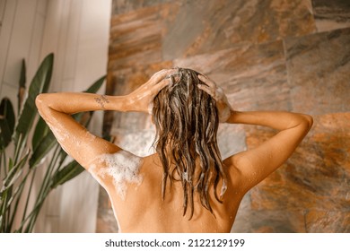 Back View Of Beautiful Naked Young Woman Taking Shower In Bathroom With Marble Tiles. Spa, Beauty And Body Care Concept. Mature Content