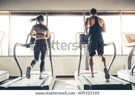 Back view of beautiful sports people running on a treadmill in gym