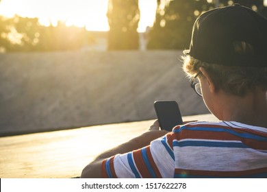 Back view of a beautiful teen using smartphone social app leaning on a concrete wall outdoor Young trendy boy watching social video online on cellphone Youth urban lifestyle and new technology concept