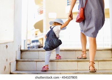 Back view of beautiful toddler girl walk with mother, stairs outdoors background, closeup view