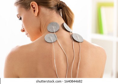 Back view of beautiful woman with electrodes on neck during electrotherapy in clinic