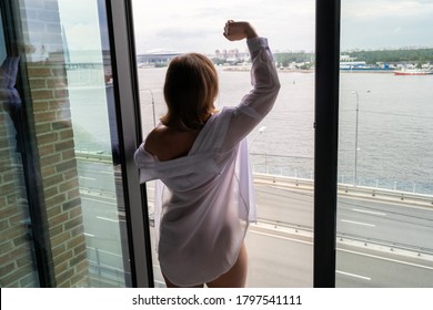 Zurück Blick auf schöne junge glückliche Frau in transparentem nächtlichem Ansehen und genießen nahe der offenen Panoramafenster der Wolkenkratzer Wohnungen. Weibliche Arme erheben sich über Stadt und Straße.