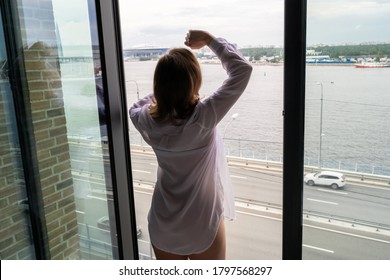 Zurück Blick auf schöne junge glückliche Frau in transparentem nächtlichem Ansehen und genießen nahe der offenen Panoramafenster der Wolkenkratzer Wohnungen. Weibliche Arme erheben sich über Stadt und Straße.